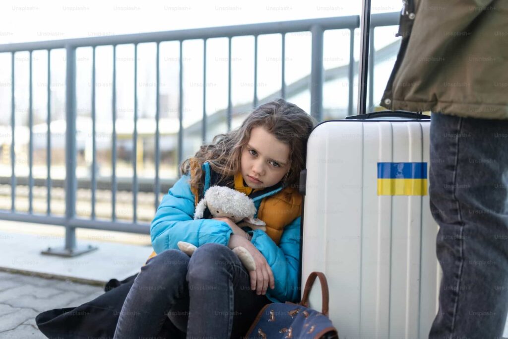 A sad Ukrainian immigrant child with luggage waiting at the train station, Ukrainian war concept. 